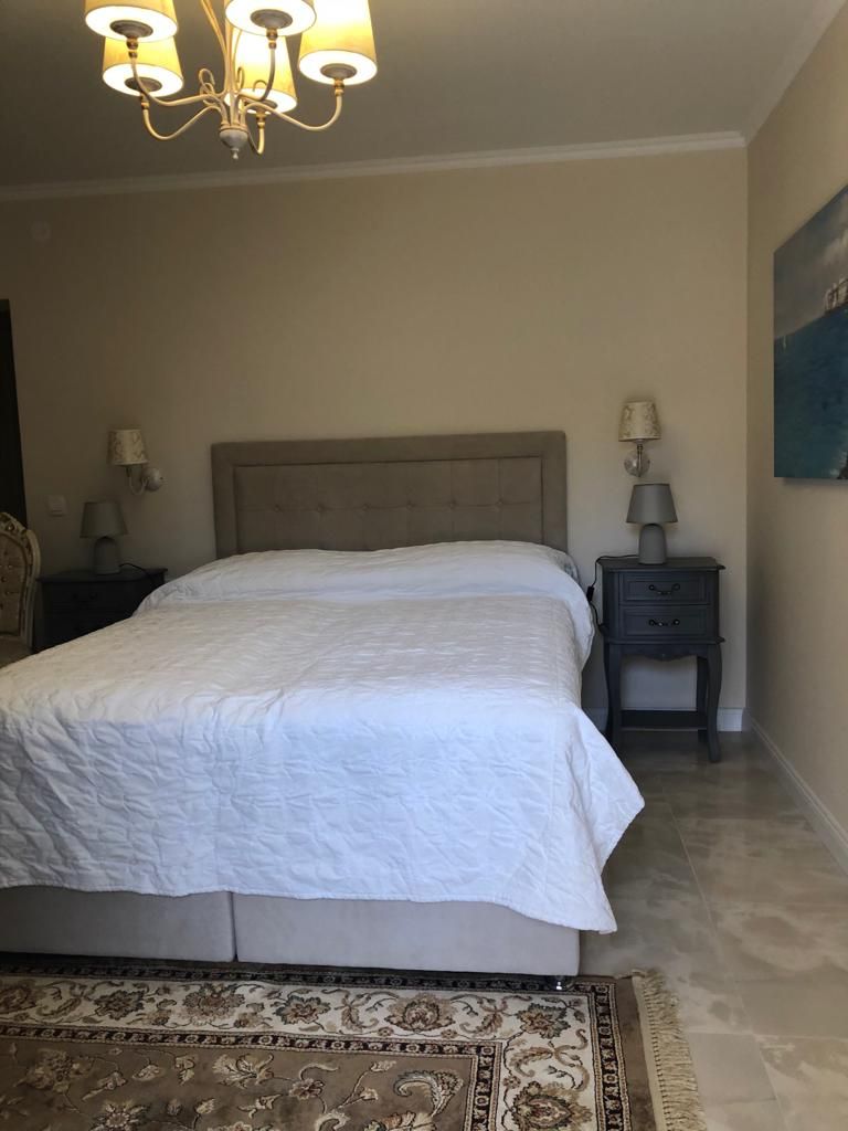 A bedroom with a bed, a nightstand, a lamp, a chandelier, and a patterned rug.