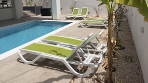 En swimmingpool med liggestole og et lille haveområde med planter og et banantræ.