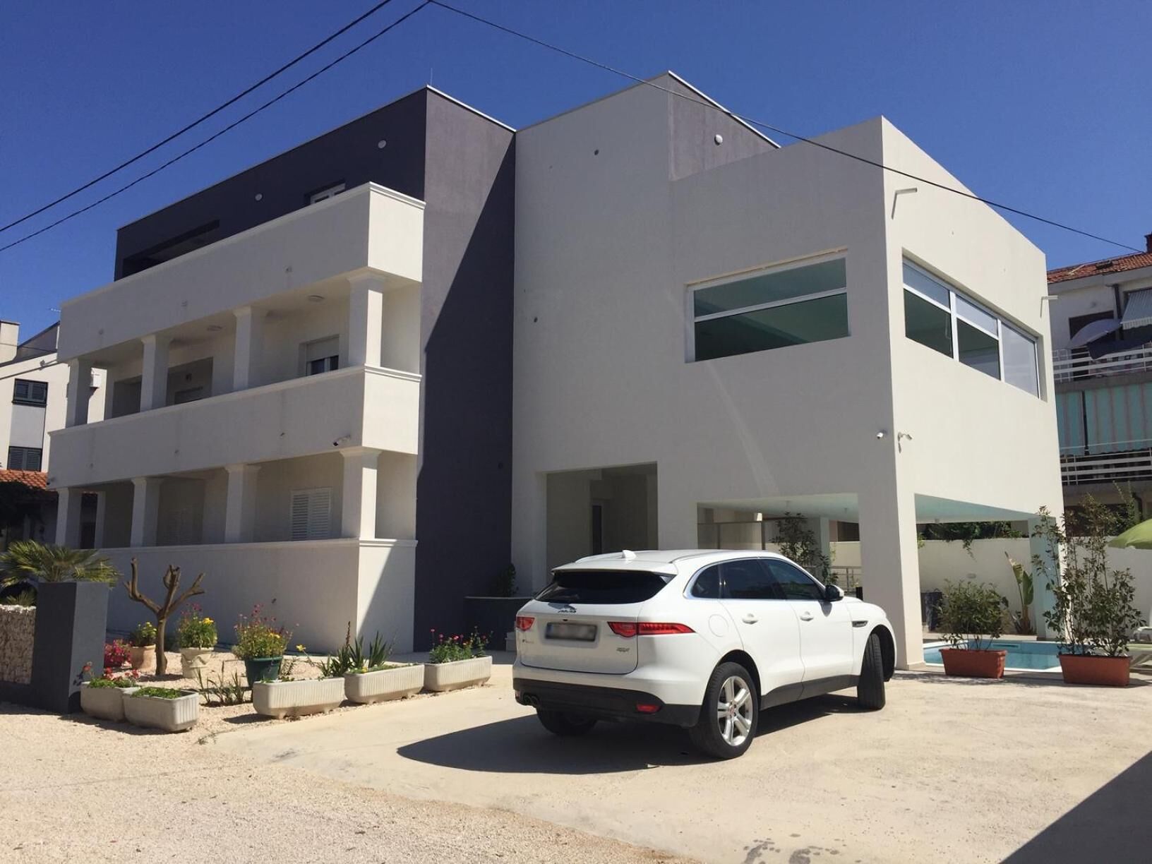 Un bâtiment moderne à deux étages, doté d’une façade blanche et d’une voiture garée dans l’allée.