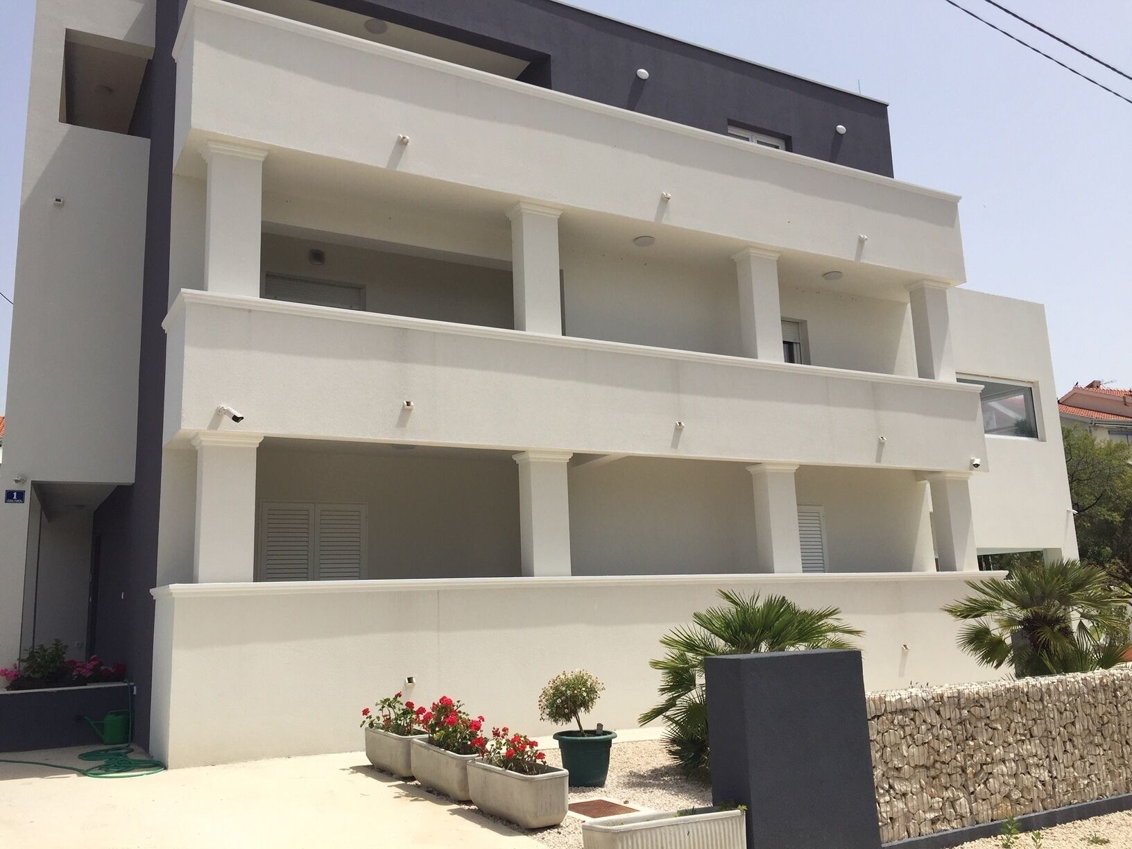 A modern two-story building with a flat roof, large windows, and a balcony on the upper floor.