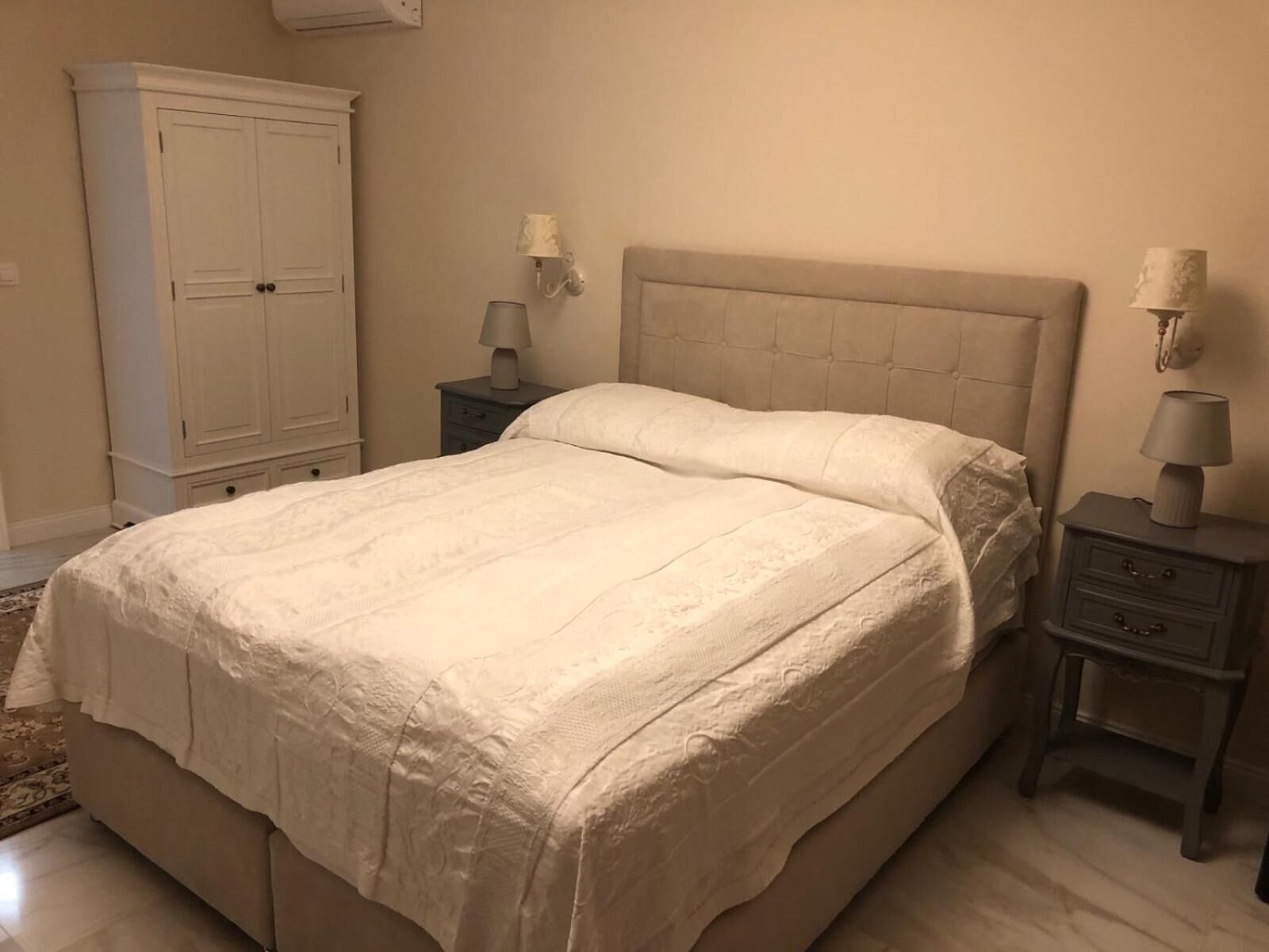 A bedroom with a bed, nightstands, a wardrobe, and wall-mounted lamps.