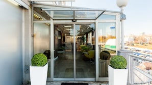 A modern building entrance with a glass door, a waiting area with seating, and potted plants. - Adresa Suites (Belgrade)