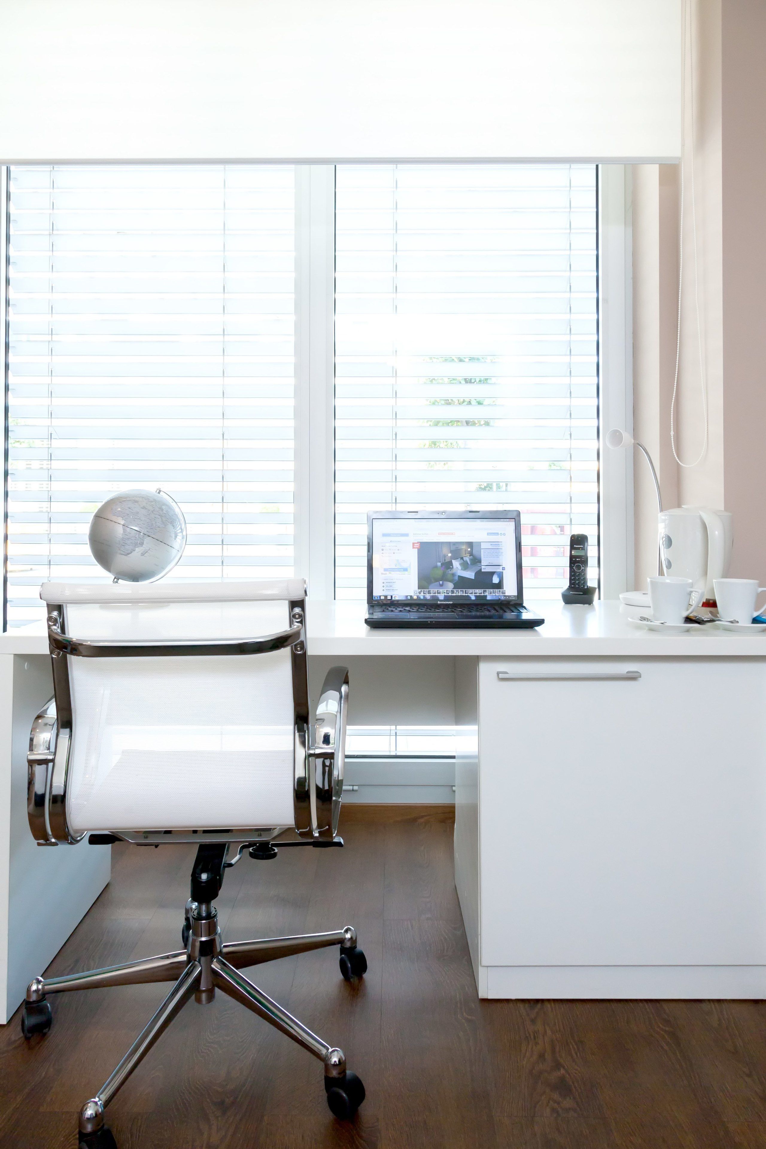 A modern office desk with a laptop, a globe, and a coffee maker.