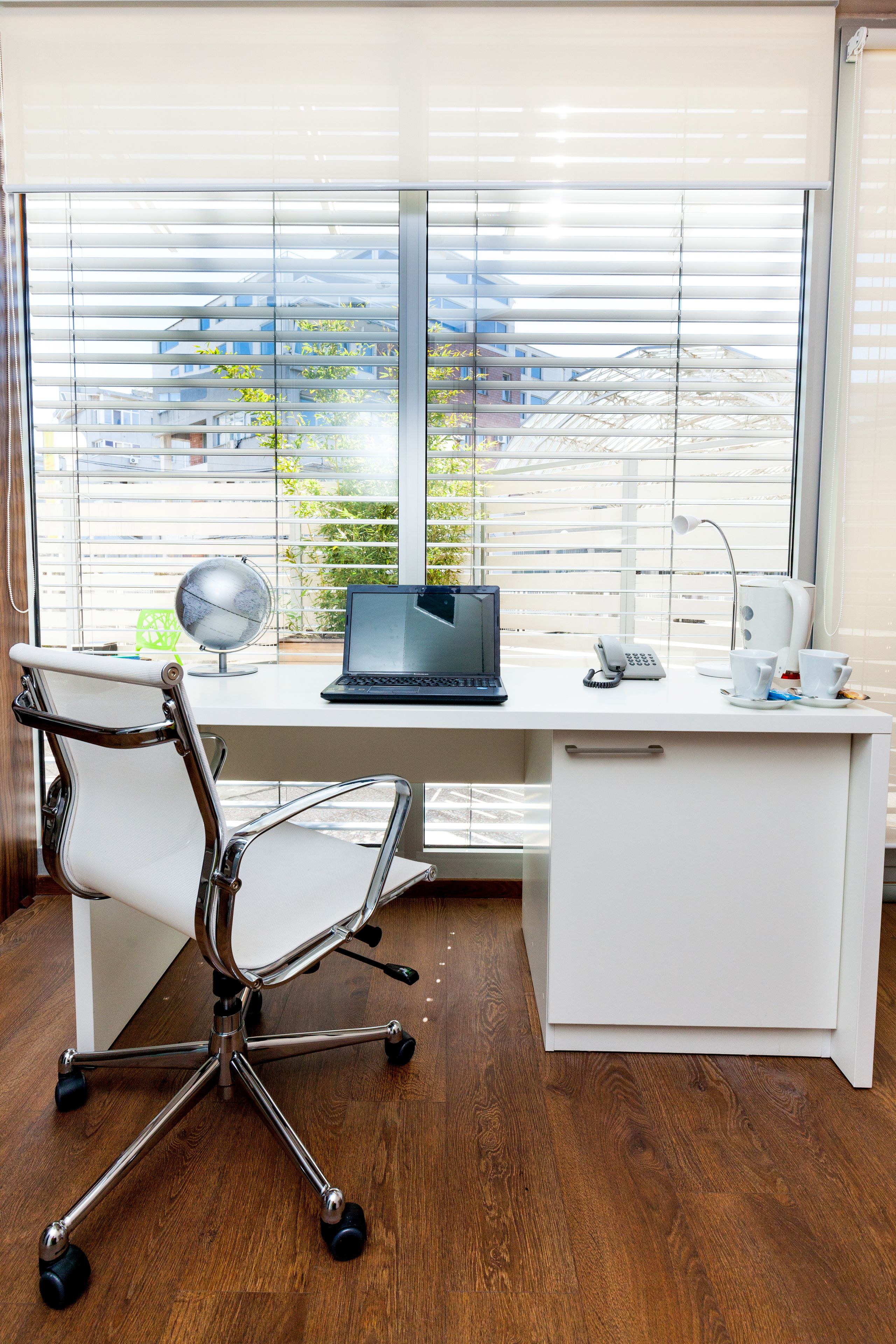 A modern office desk with a laptop, a globe, a telephone, and a cup.