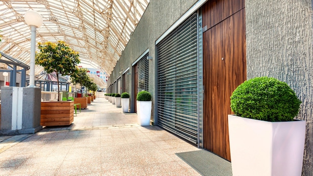 A covered walkway with planters and benches, leading to a building with closed shutters. - Adresa Suites (Belgrade)