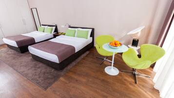 A hotel room with two beds, a small table with fruit, and a green chair.