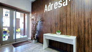A reception area with a wooden wall, a white reception desk, and a glass door entrance. - Adresa Suites (Belgrade)