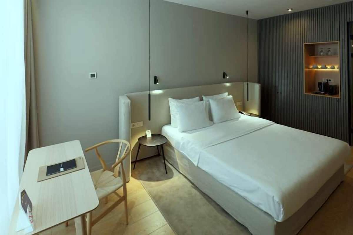 Una habitación de hotel moderna con una cama grande, mesitas de noche, un escritorio pequeño y una silla.