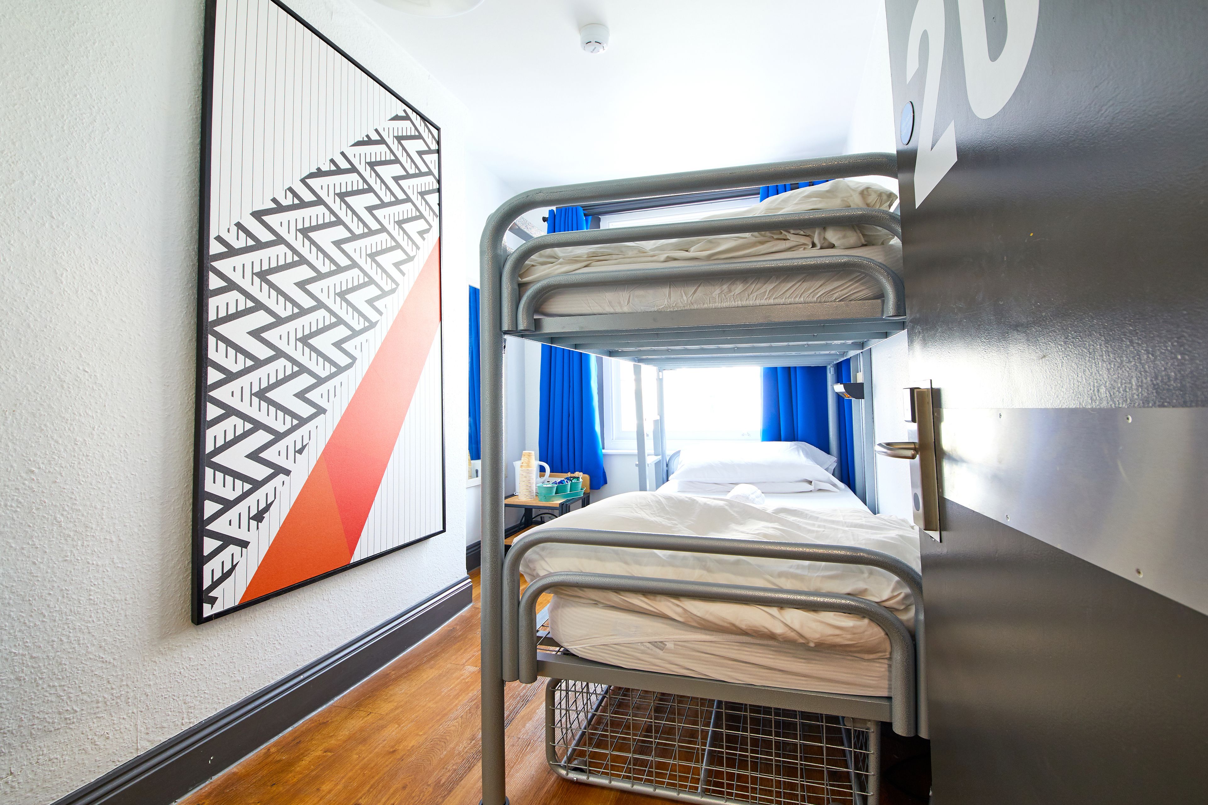 A bunk bed in a room with a geometric patterned wall art, a window with blue curtains, and a visible door handle.
