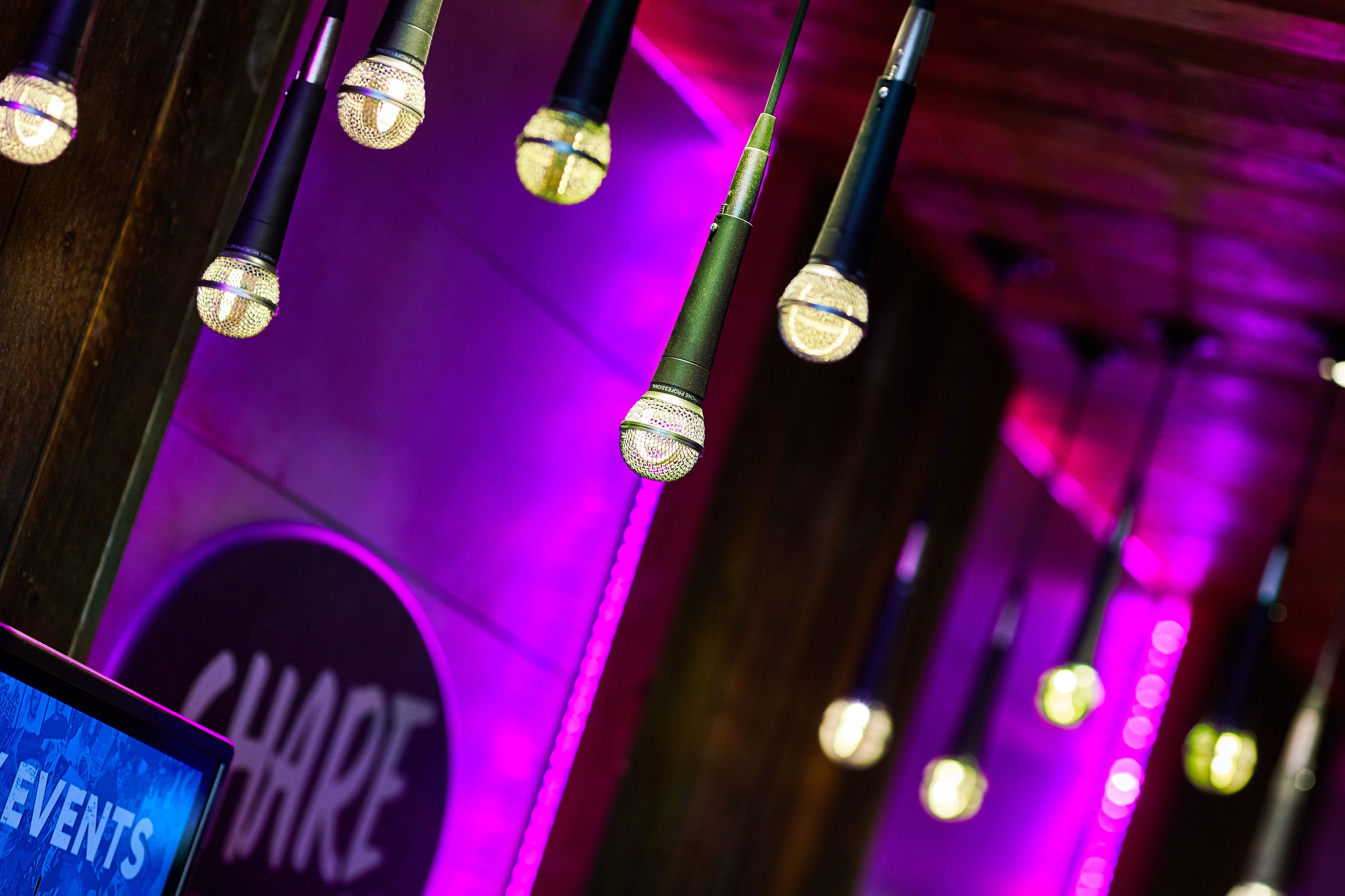 Una fila de micrófonos con un fondo iluminado en morado y un letrero que dice 'SHARE EVENTS'.