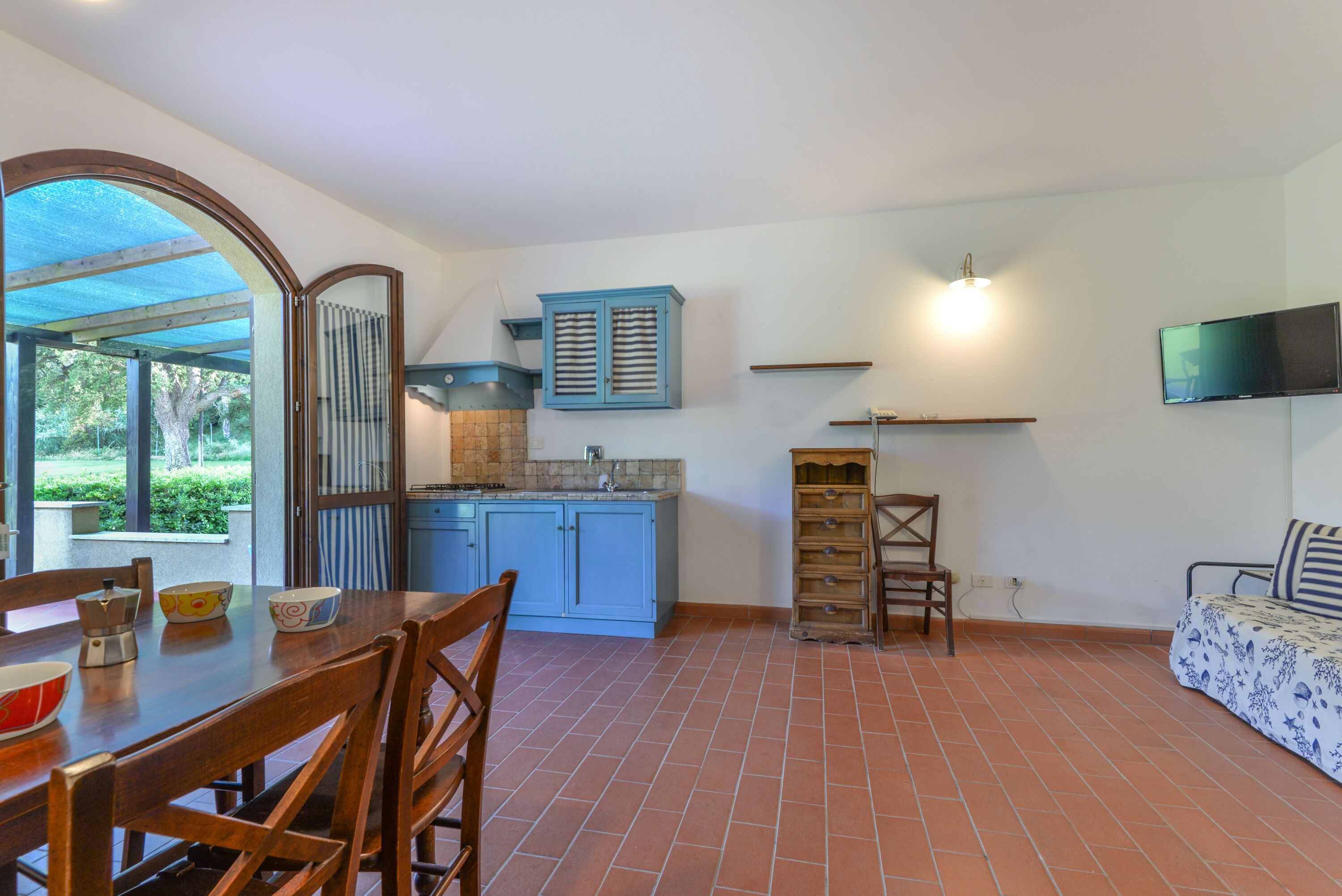 A kitchen with blue cabinets, a dining table with chairs, and a TV mounted on the wall.