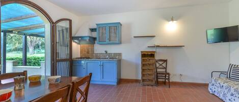 A kitchen with blue cabinets, a dining table with chairs, and a TV mounted on the wall.