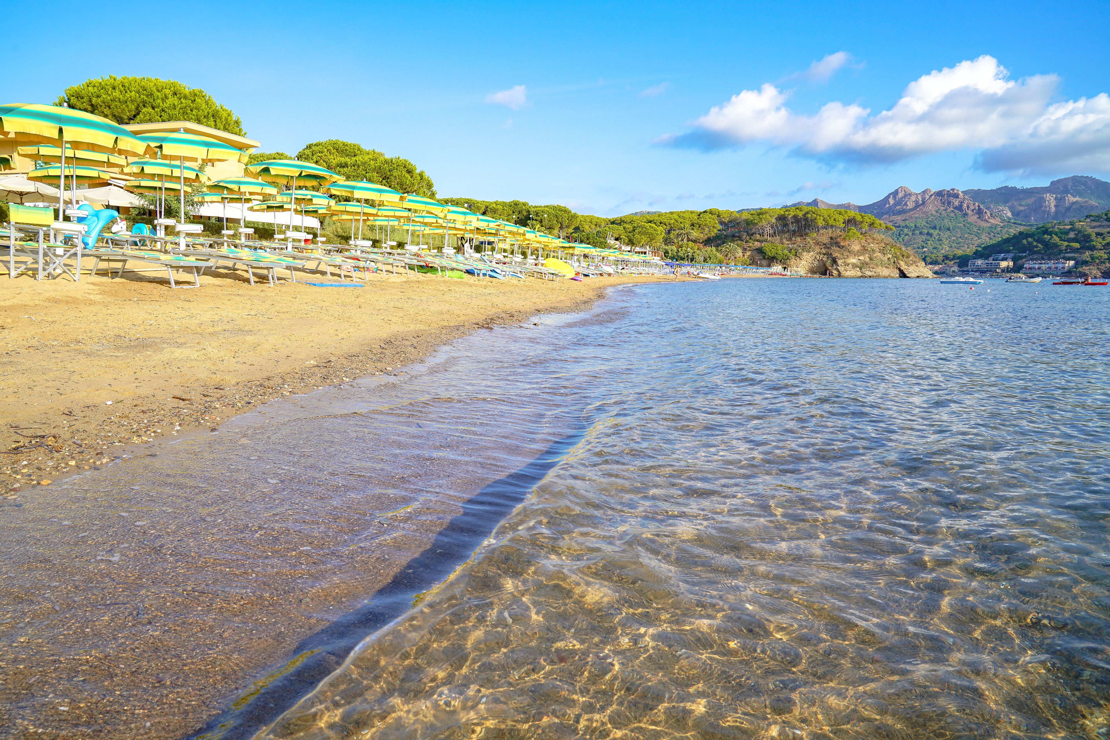 Una playa con aguas transparentes y poco profundas, sombrillas y sillas reclinables.