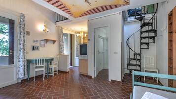 Un'ampia stanza con pavimento piastrellato, un'area pranzo con sedie, una scala e un soffitto con decorazioni.