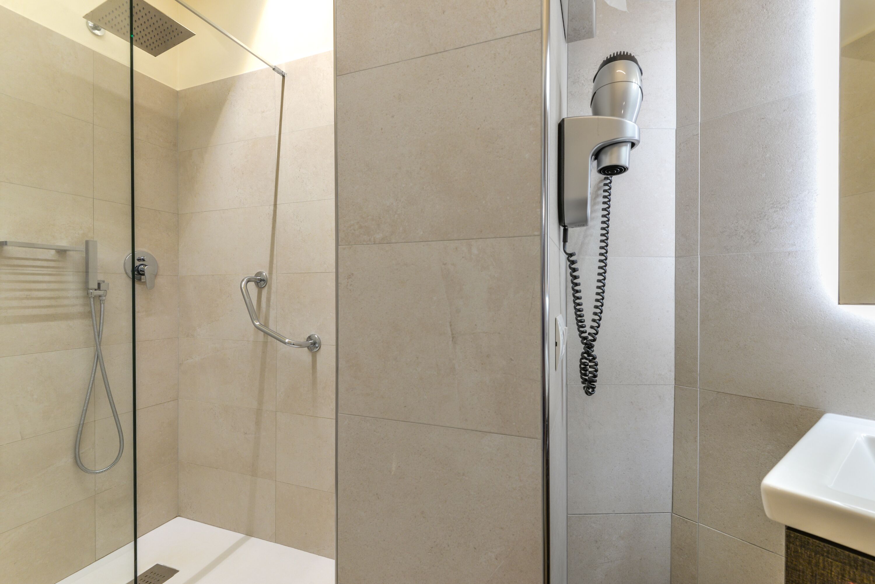 Een moderne badkamer met een douchecabine van glas, een handdouche en een föhn aan de muur.