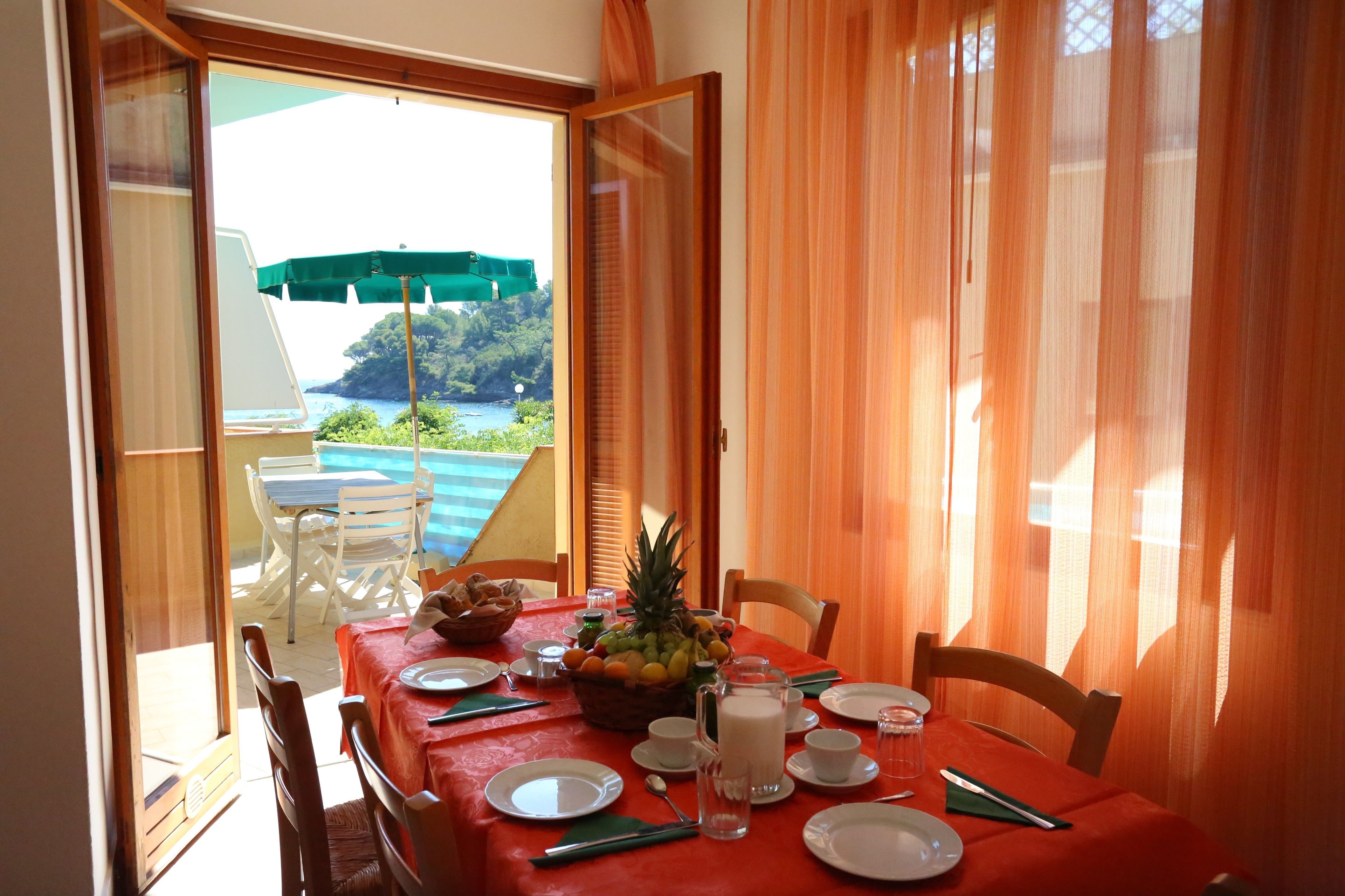 Un coin repas avec une table dressée pour deux personnes, un panier de fruits et une carafe de lait.