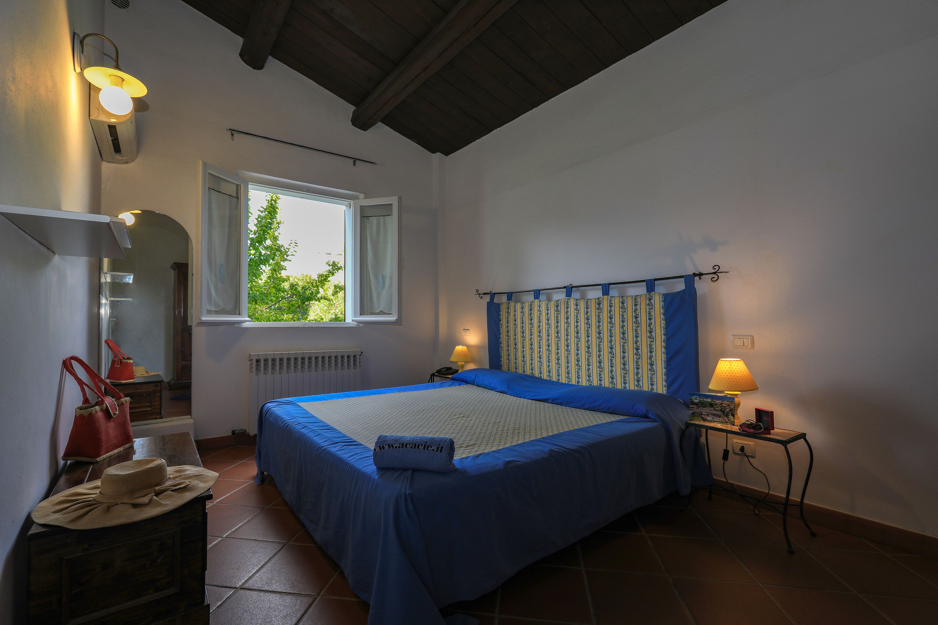 Un dormitorio con cama, lámparas de noche, mesita de noche, ventana y cómoda.