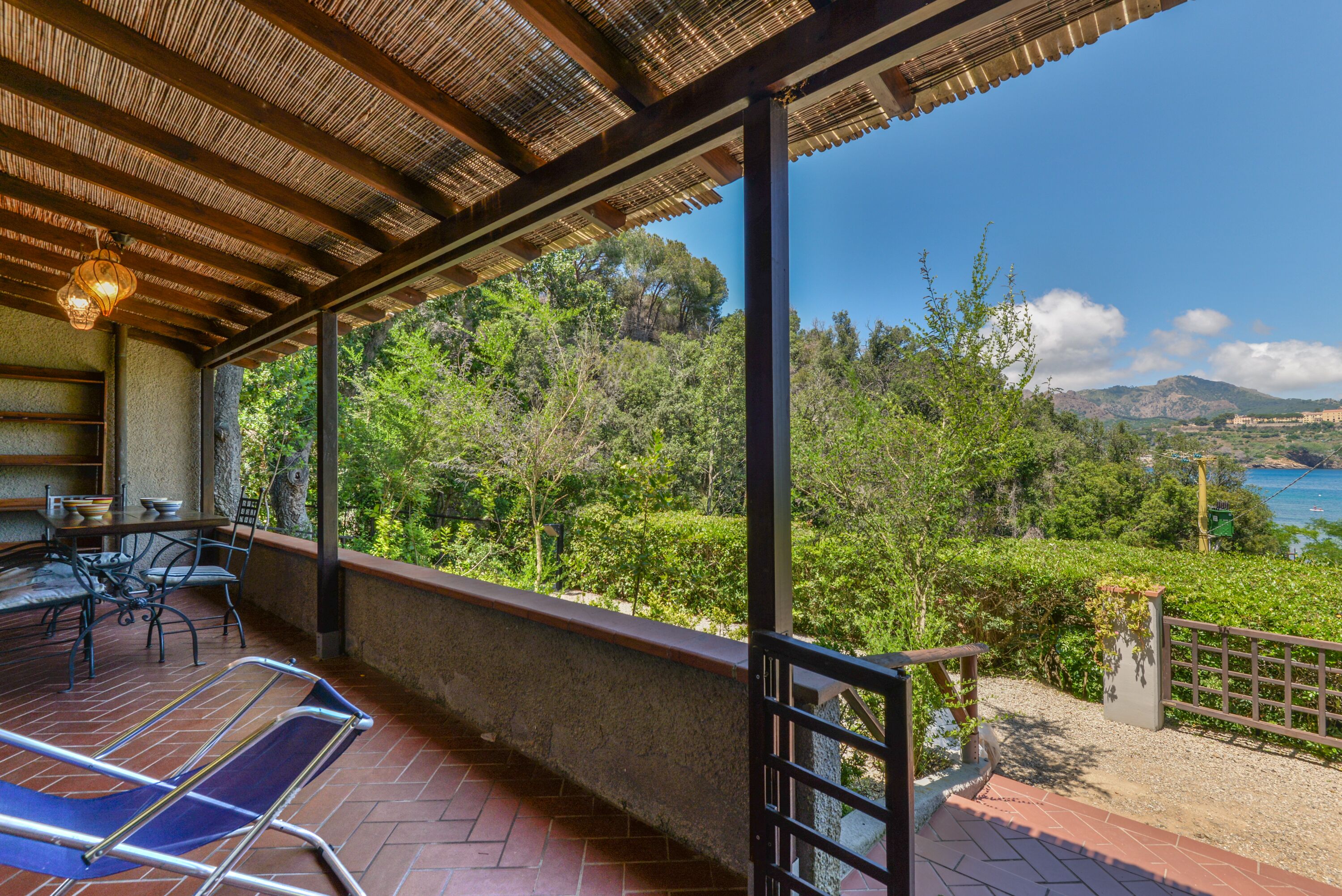 A covered outdoor area with a table and chairs, overlooking a scenic landscape with trees and a body of water.