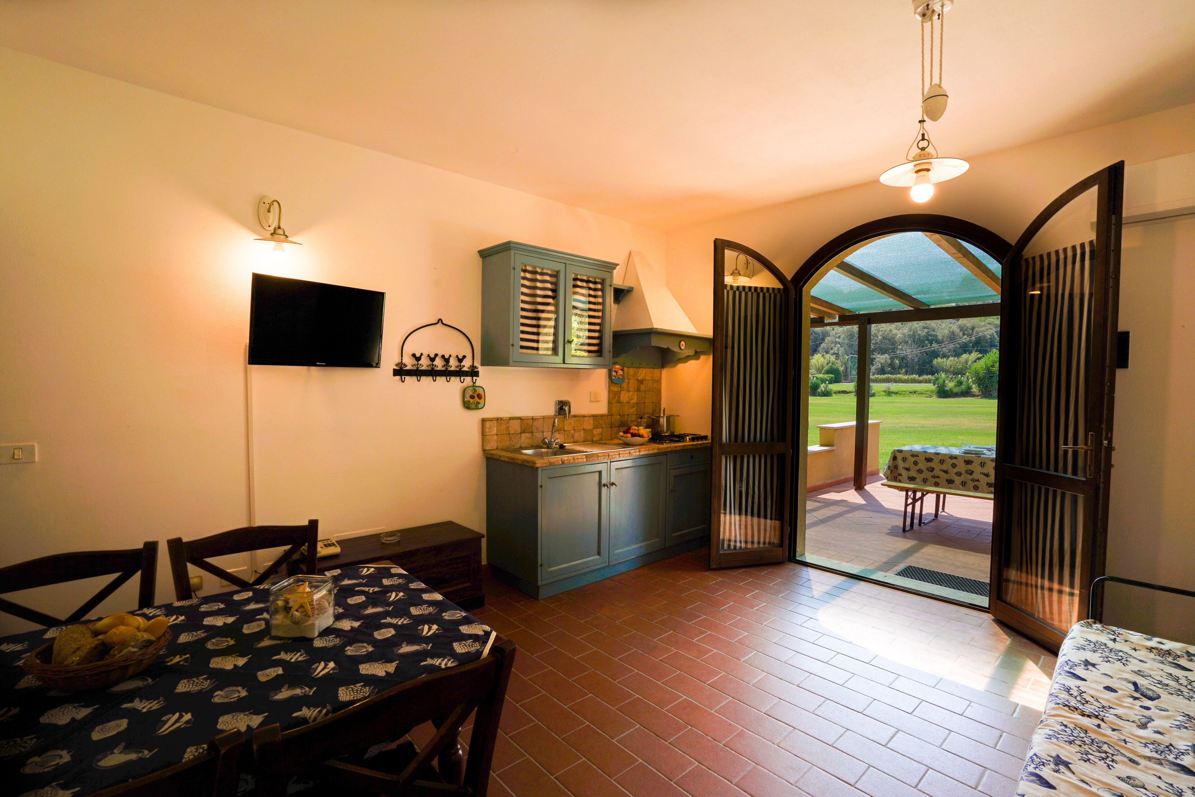 A compact kitchen with a dining area, a TV, and a view through an open door to an outdoor patio.