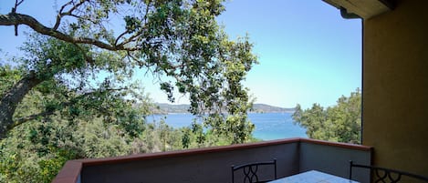 A balcony with a tiled table and chairs, overlooking a body of water and greenery.