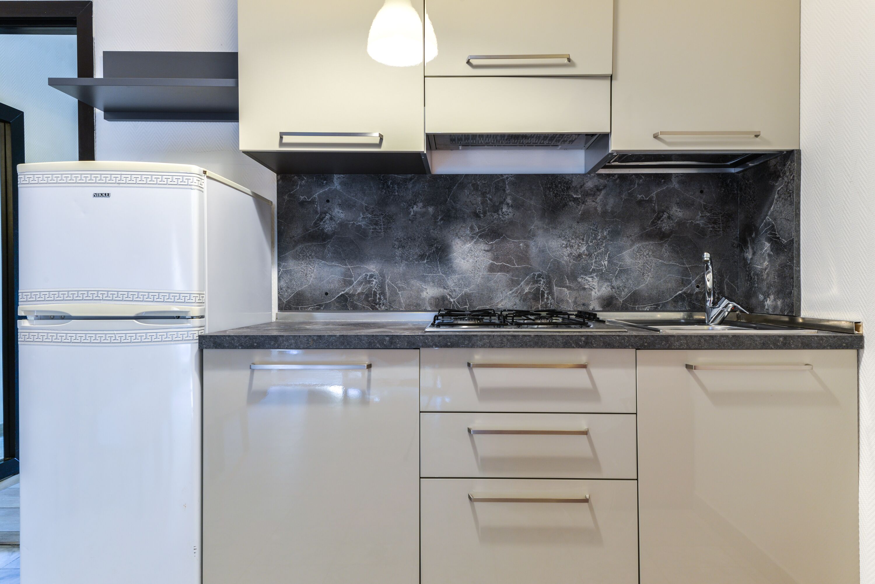 A modern kitchen with white cabinets, a black marble backsplash, and a built-in stove.