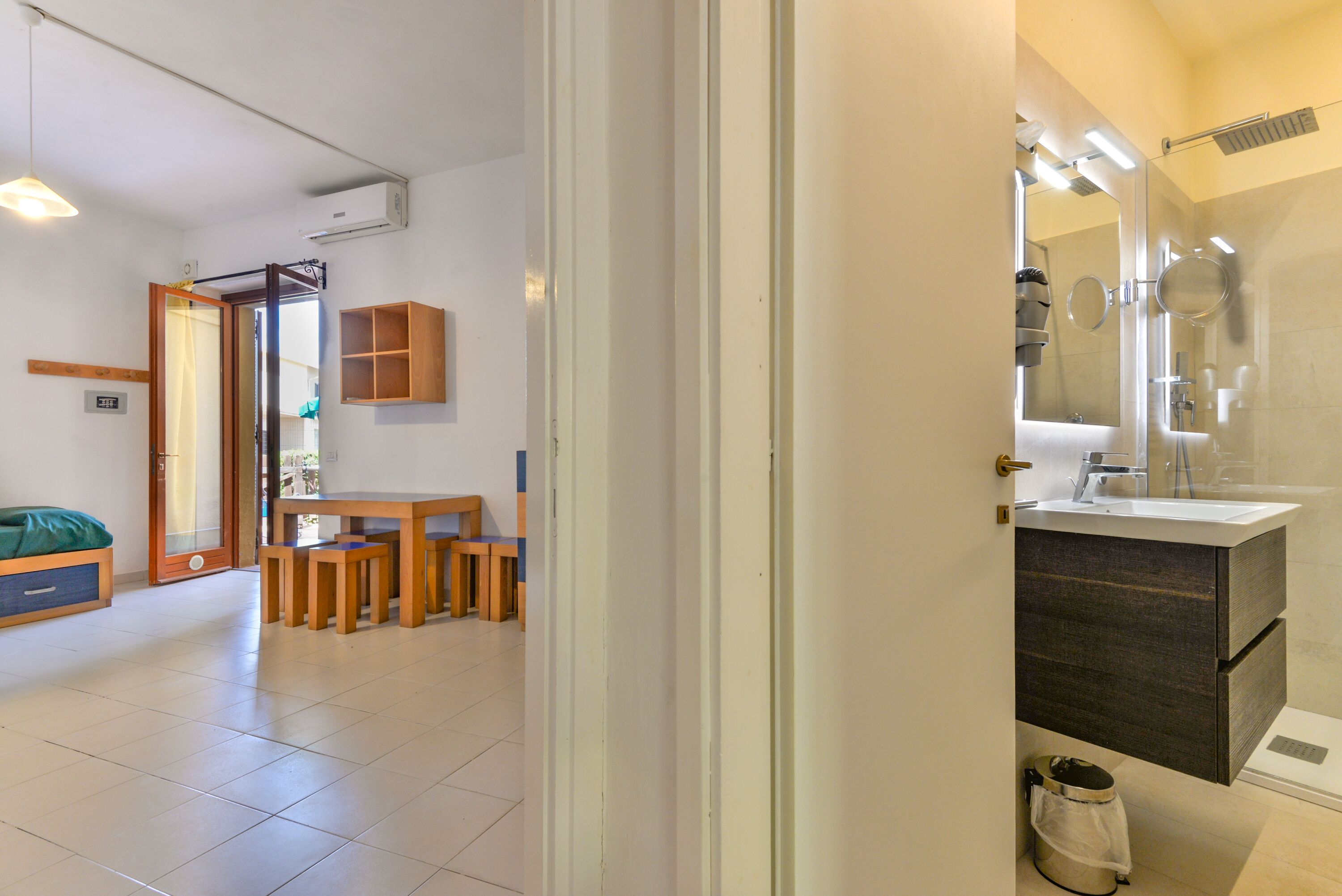 Une salle de bain moderne avec un grand miroir, un lavabo et une douche. On trouve une petite poubelle sous le lavabo.