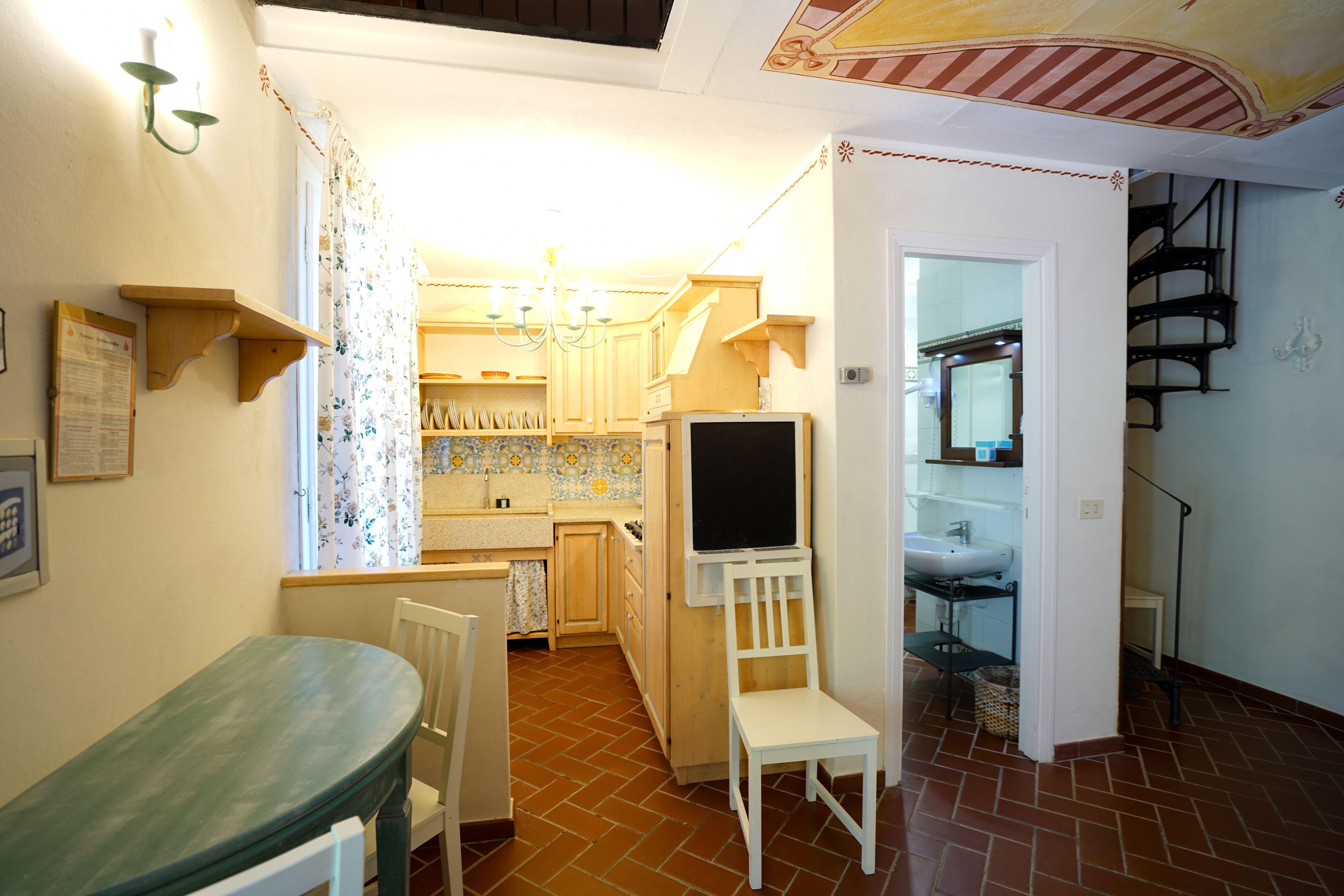 A compact kitchen with a dining area, a TV, and a staircase leading to an upper level.