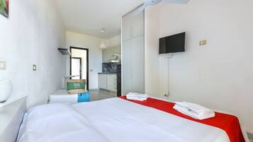 Una habitació d'hotel amb un llit, una paret vermella decorativa, un ventilador de sostre, una televisió i vista a la zona de la cuina.