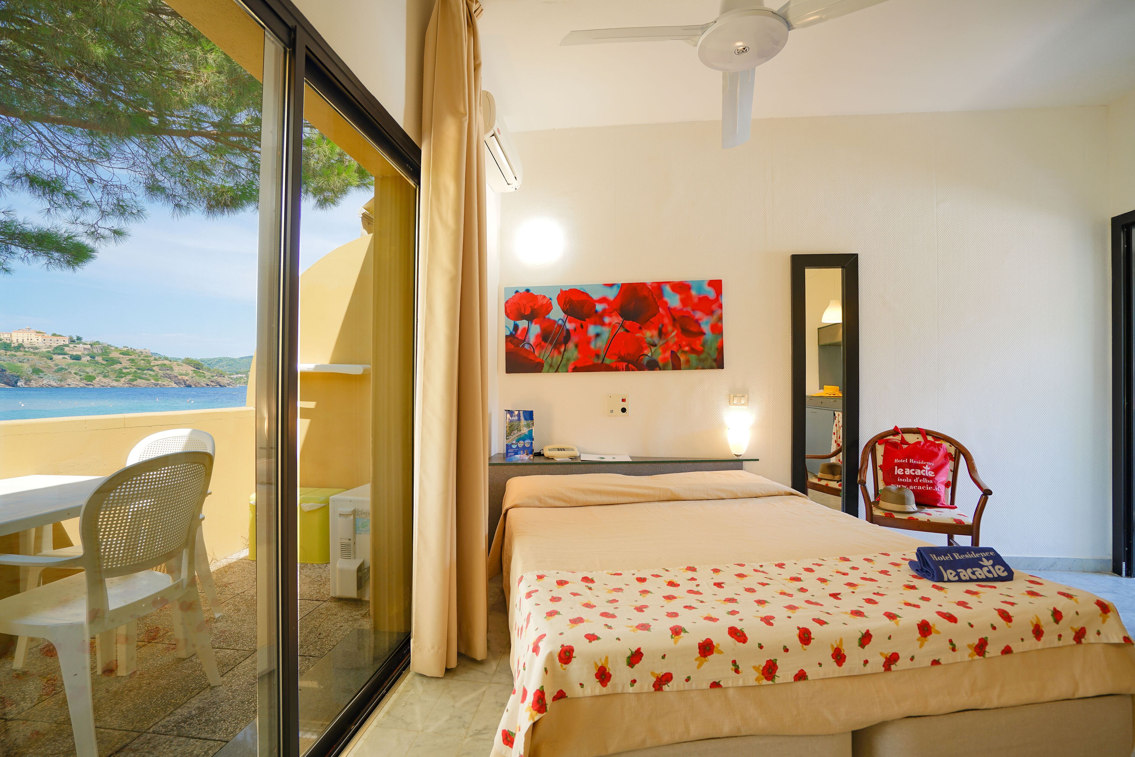 A hotel room with a bed, a desk, a chair, and a view of the sea.