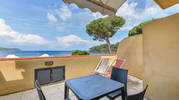A balcony with a table and chairs, overlooking a scenic view of the sea and a tree.