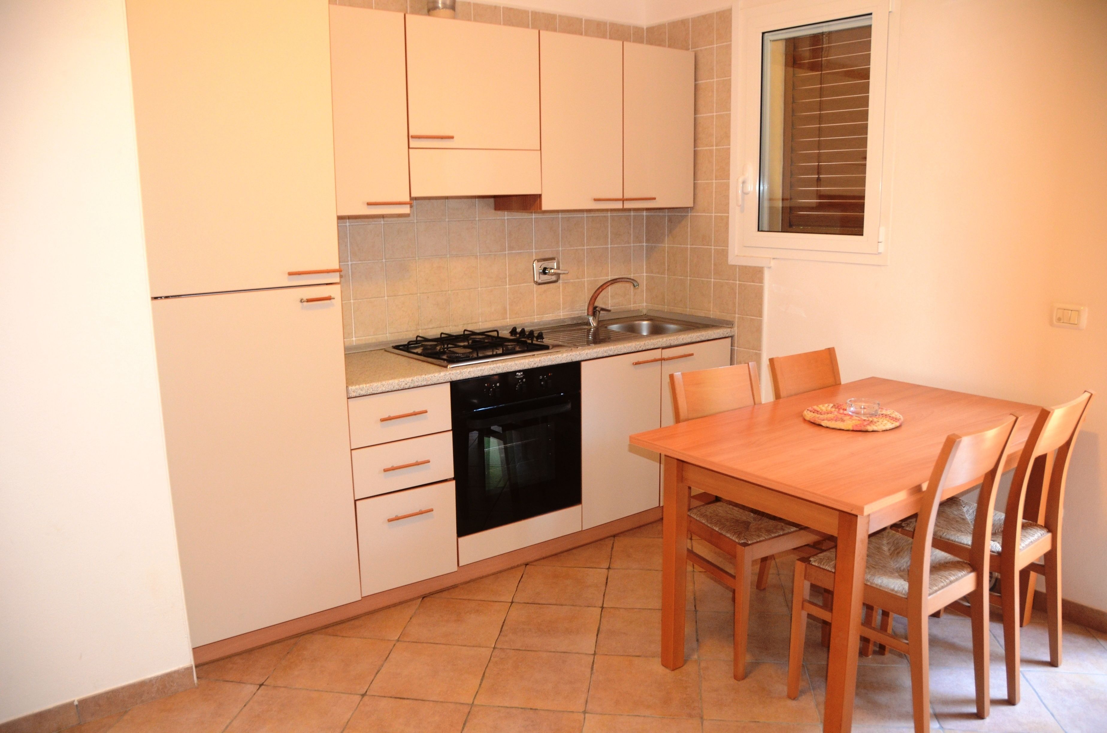 Una cocina compacta con armarios blancos, estufa a gas, horno empotrado y una mesa con sillas.