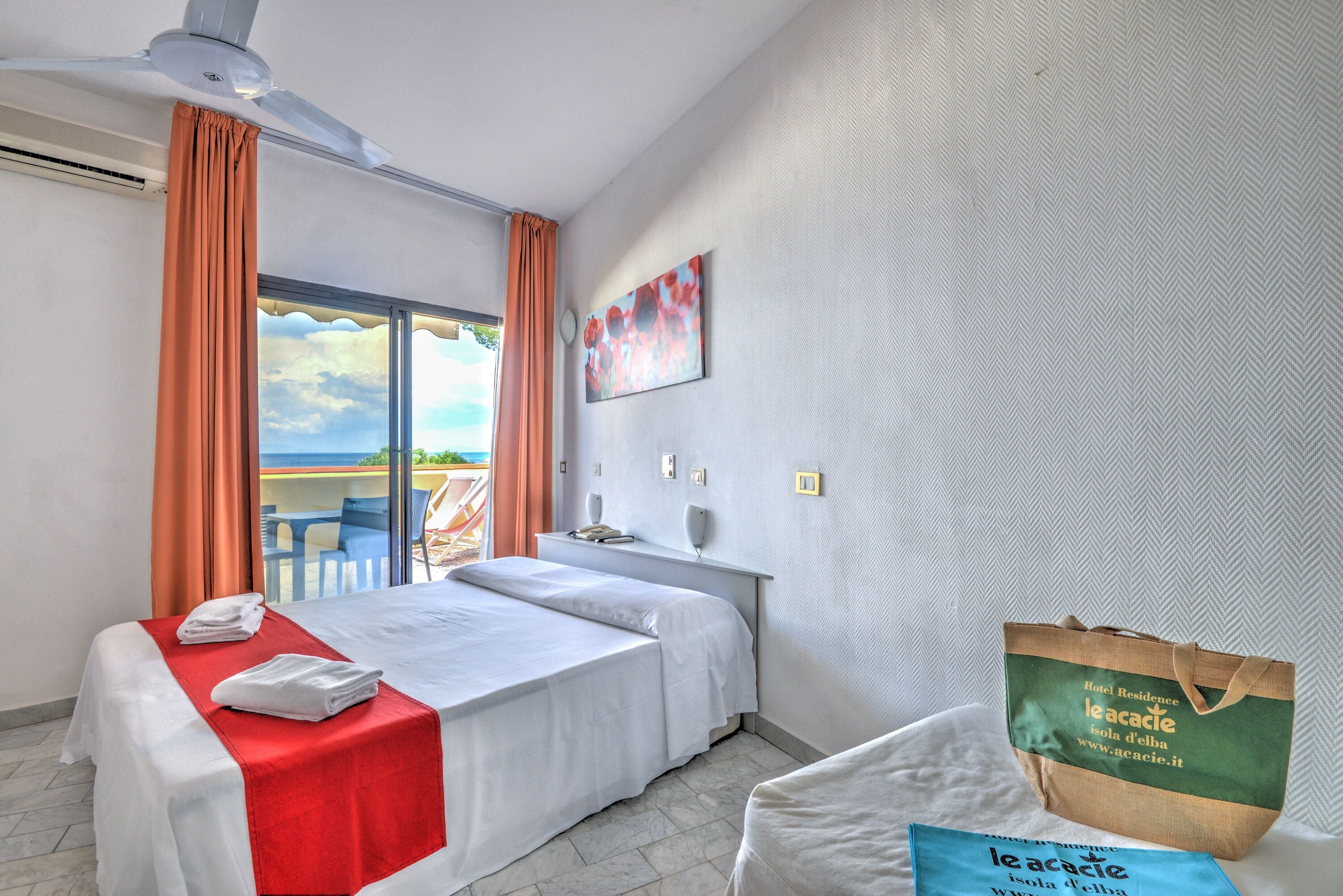 A hotel room with two beds, a balcony, a painting, and a branded tote bag.