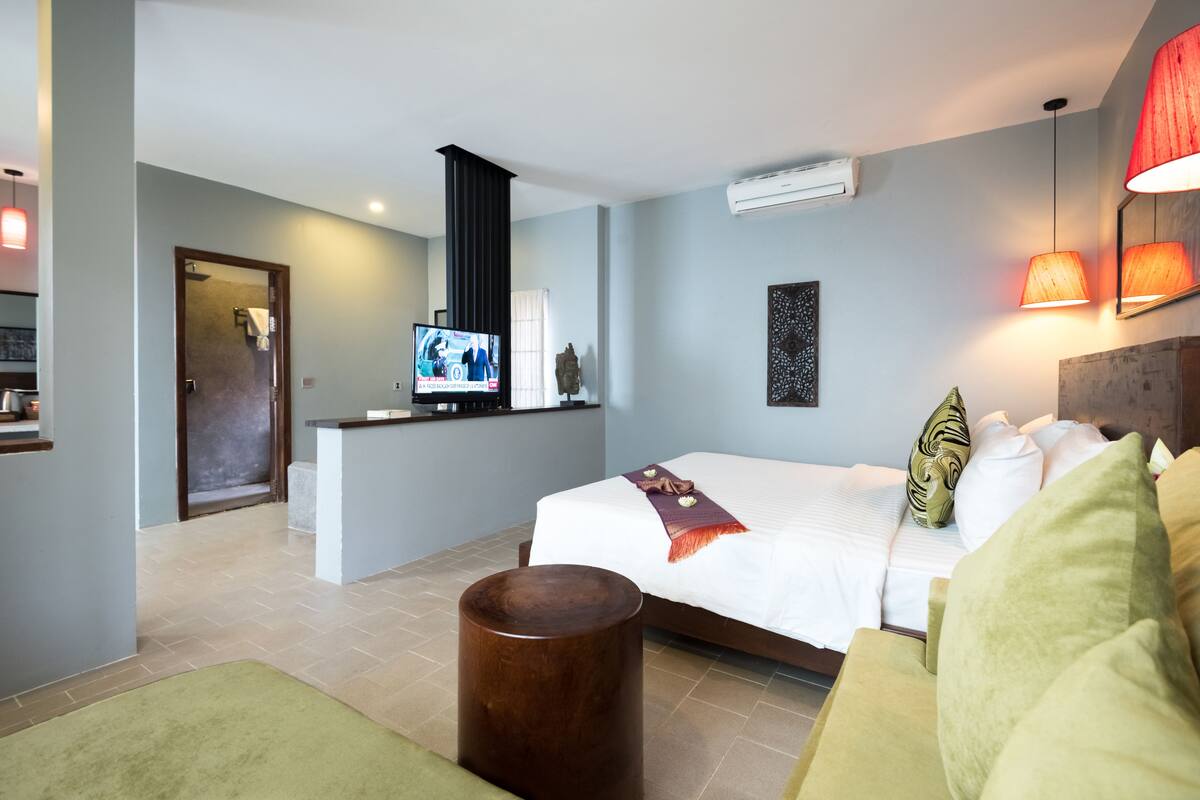 A hotel room with a bed, a TV, a small kitchen area, and a bathroom.