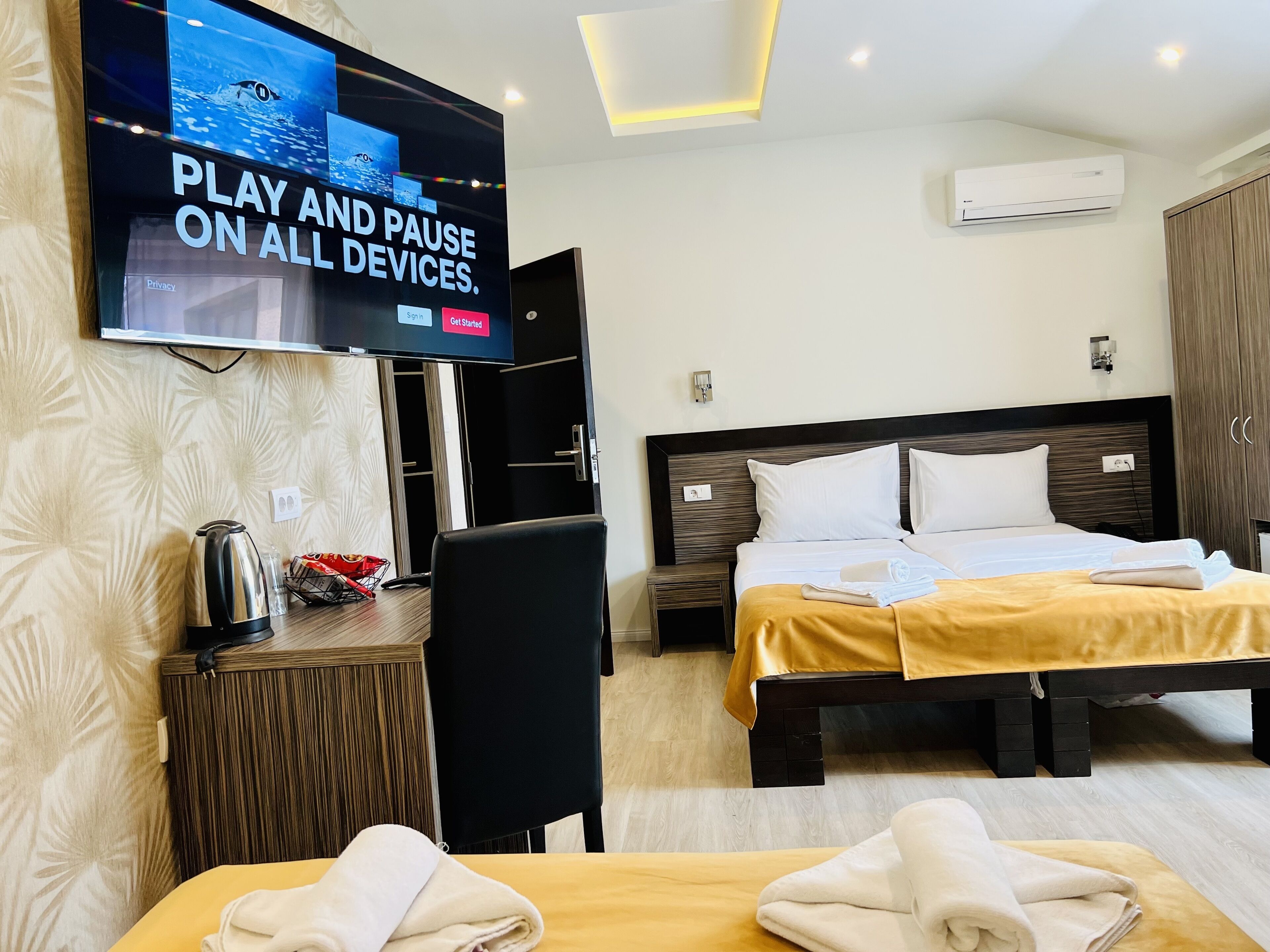 Camera d'albergo con due letti, una TV a parete, una macchina del caffè e un tavolino con un bollitore e un cesto.
