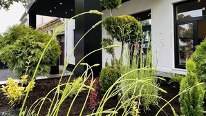 Entrada de hotel con diseño moderno, incluyendo un cartel llamativo y un jardín ajardinado con diversas plantas.