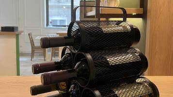 A wine rack with multiple bottles on a wooden table in a room with a modern design, including a hanging light fixture and a window with a view.