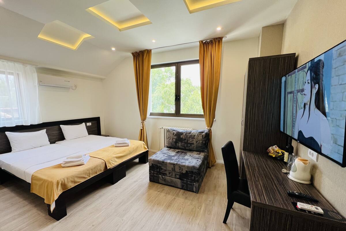 Quarto de hotel com uma cama, uma escrivaninha com televisão e uma janela com cortinas.