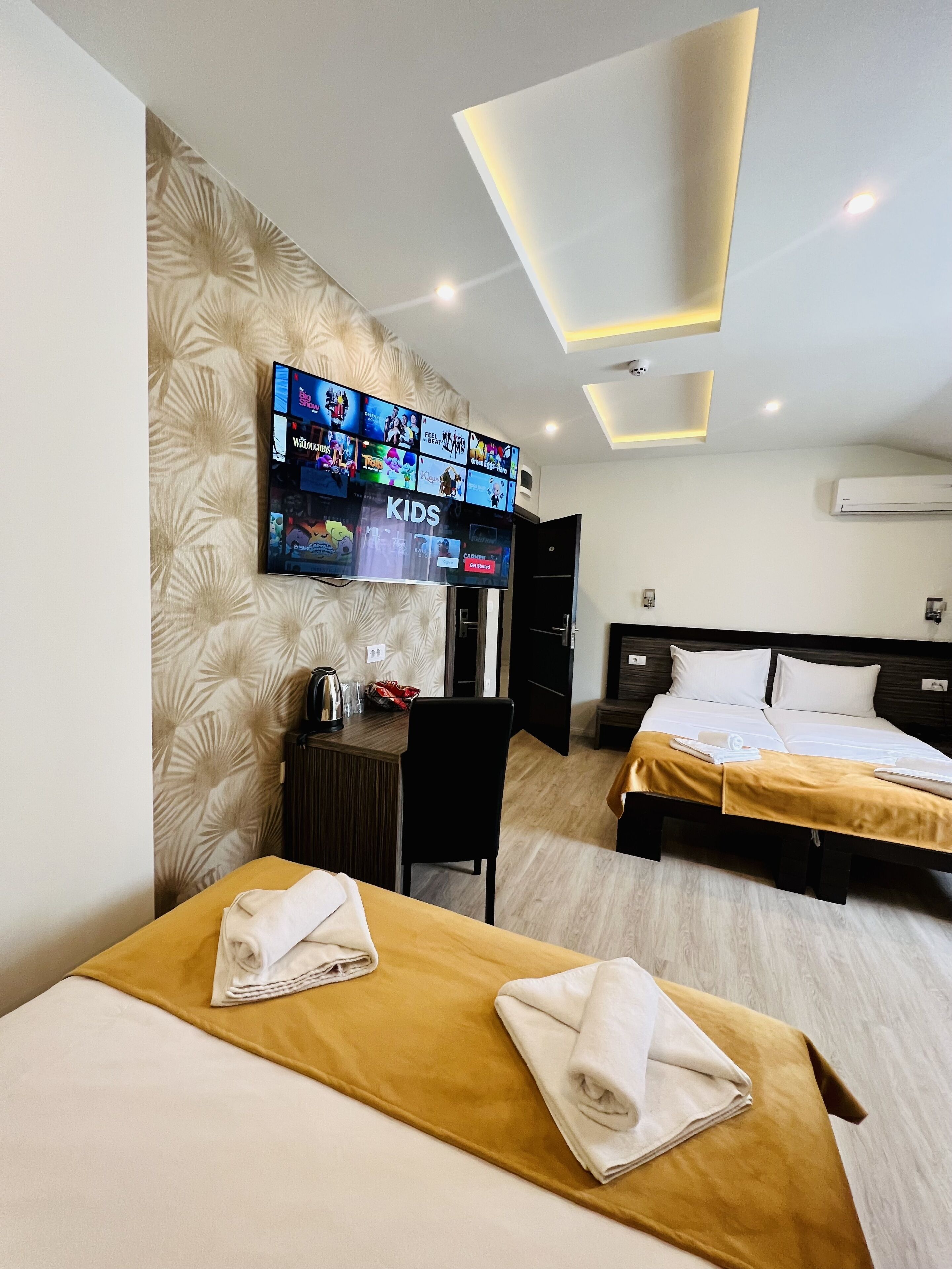 Ein Hotelzimmer mit zwei Betten, einem Schreibtisch und einem Flachbildfernseher, der Kindersendungen zeigt, sowie einem modernen Deckenstil.