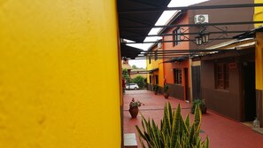 A narrow alleyway with a yellow wall on one side and a red-tiled path. There are potted plants and a white car parked in the background. - Terra Iguazú Apart Hotel (Puerto Iguazú)