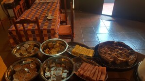 A dining area with a checkered tablecloth, metal bowls with various food items, and a large dish of meat. - Terra Iguazú Apart Hotel (Puerto Iguazú)