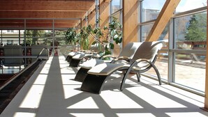 Un espacio interior iluminado por el sol con sillones de descanso y una piscina.