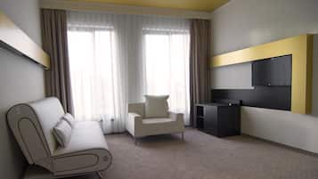 Una habitación de hotel moderna con sofá, sillón, televisión de pantalla plana y un amplio ventanal con cortinas.