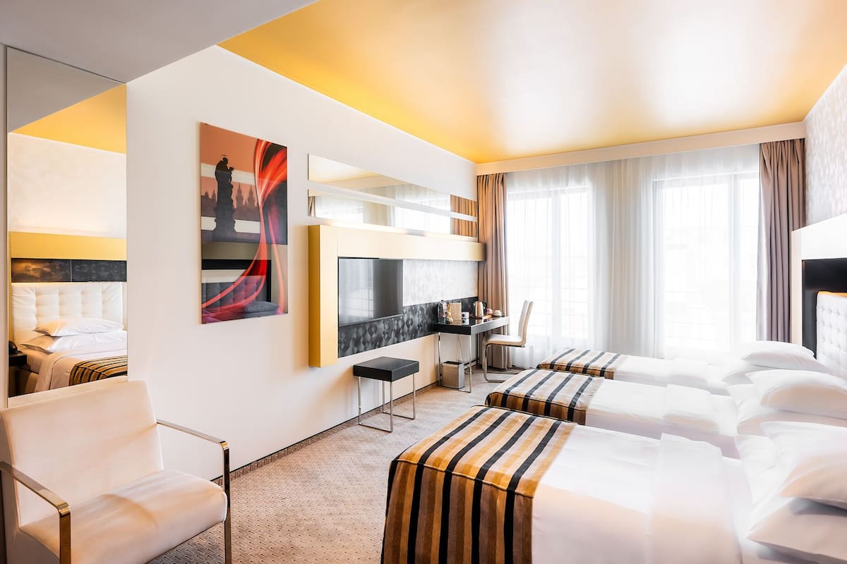 A hotel room with two beds, a desk, a chair, and a large window with curtains.