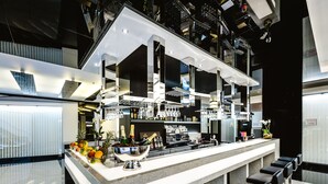 A modern bar area with a long counter, multiple bar stools, and a variety of bottles and glasses.