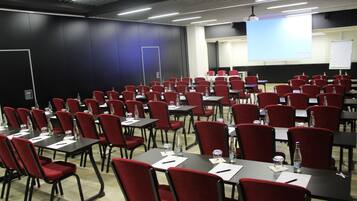 Uma sala de conferências com fileiras de cadeiras vermelhas e mesas, equipada com garrafas de água e cartões de identificação.