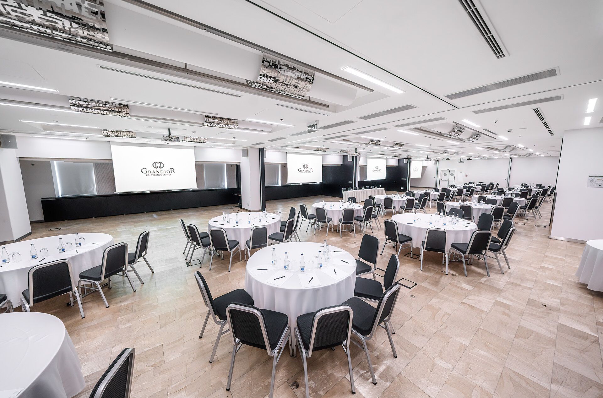 Un salón de conferencias con varias mesas redondas, cada una con sillas y botellas de agua.