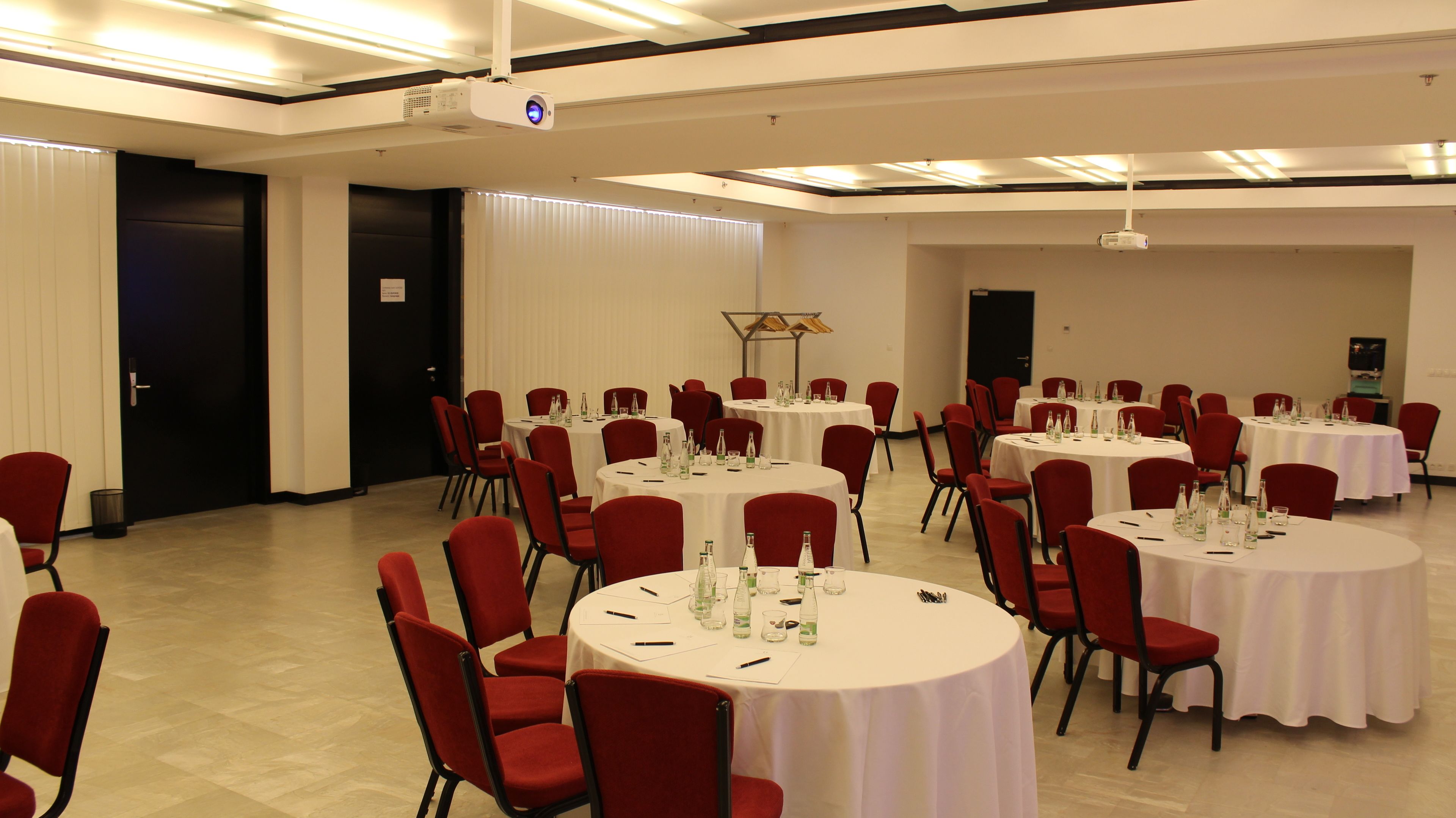 A conference room with multiple round tables, red chairs, and white tablecloths.