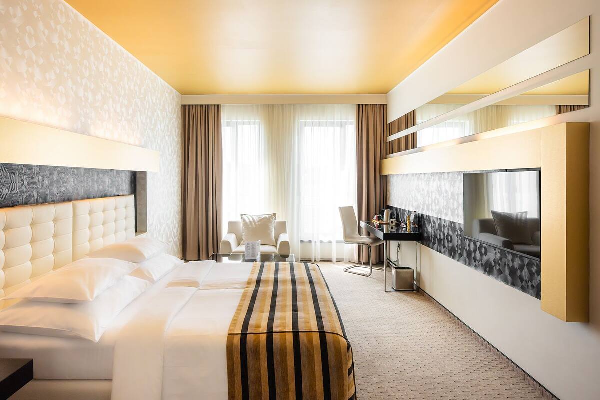 A hotel room with a large bed, a sofa, a TV, and a desk with a chair.