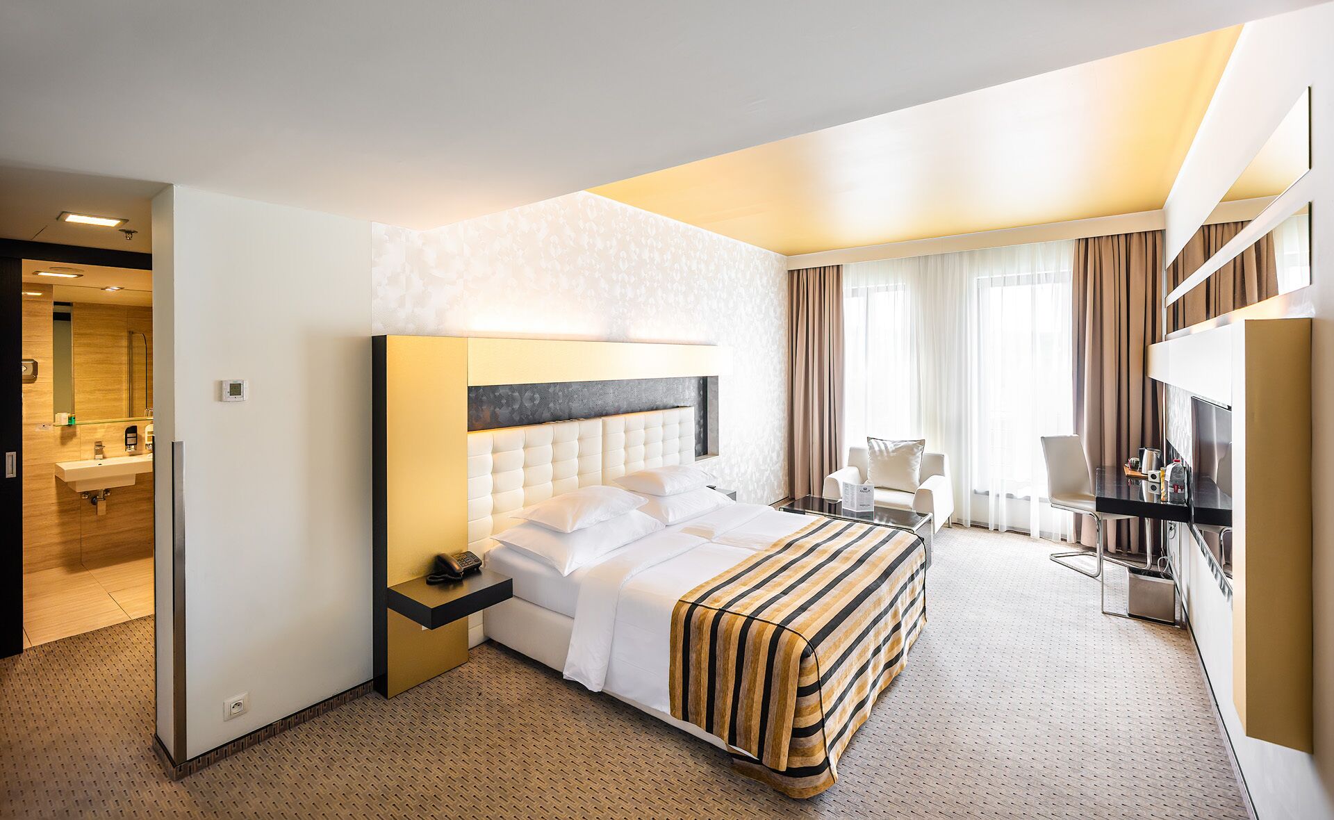 A hotel room with a large bed, a desk, a chair, and a TV.
