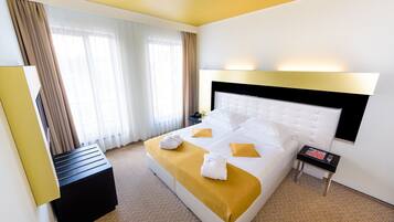 Quarto de hotel com uma cama grande, mesa de cabeceira, luminária e vista para o exterior pela janela.